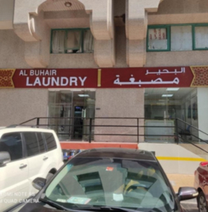 Exterior storefront of Al Buhair Laundry with maroon signage in English and Arabic.